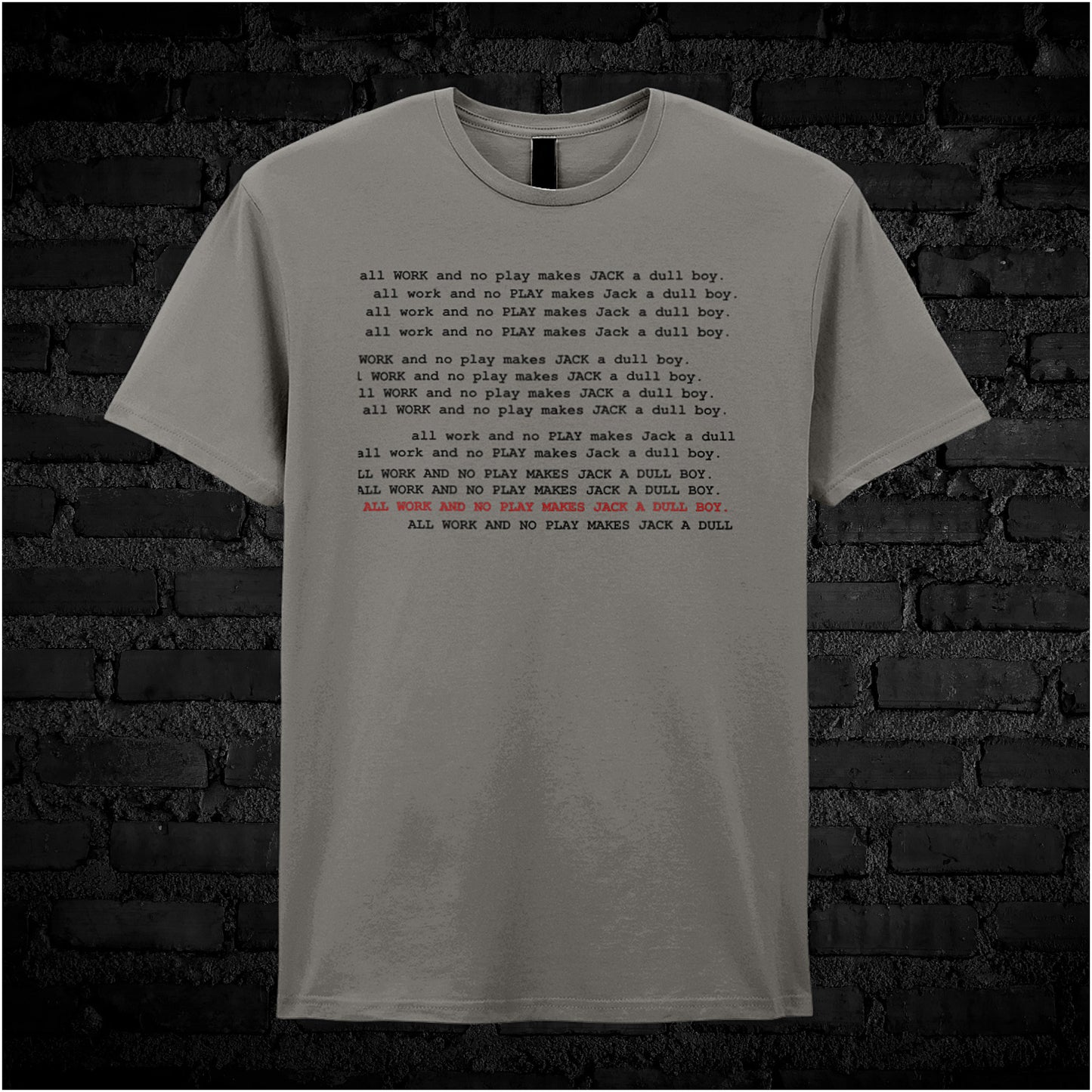 Charcoal unisex t-shirt featuring the phrase “All Work And No Play Makes Jack A Dull Boy” inspired by the movie The Shining, displayed in bold, black typewriter-style lettering.