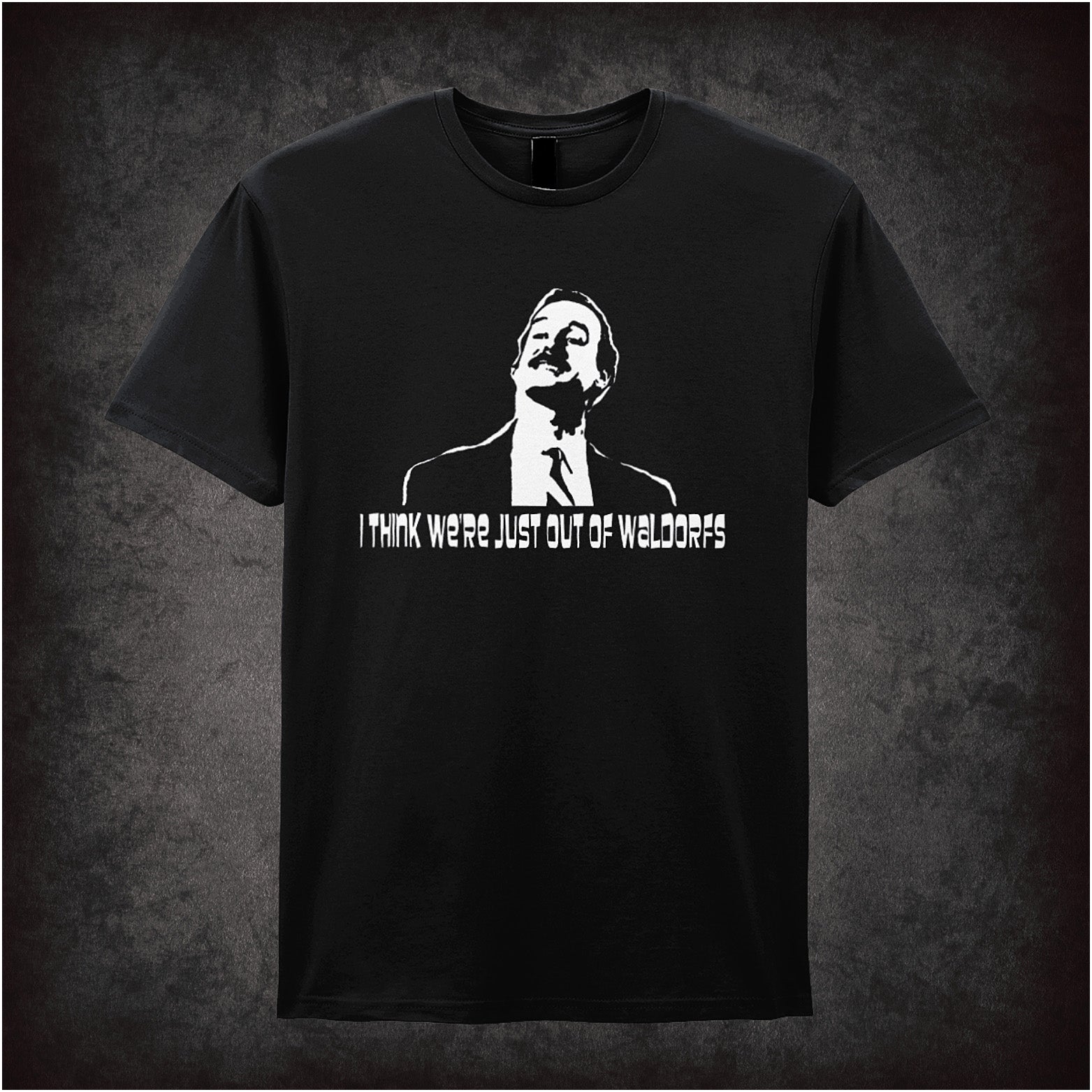 Soft style black unisex T-shirt featuring the quote "I Think We're Just Out of Waldorfs" inspired by Fawlty Towers, printed in bold, classic lettering.